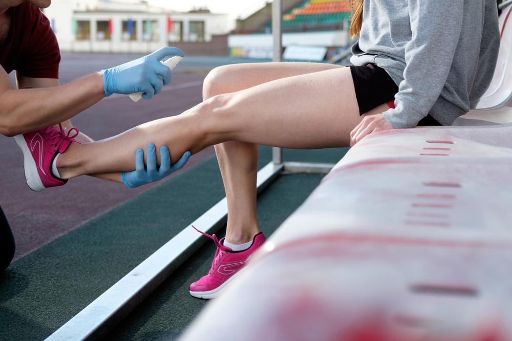 A coach spraying analgesic spray on a female runner's leg